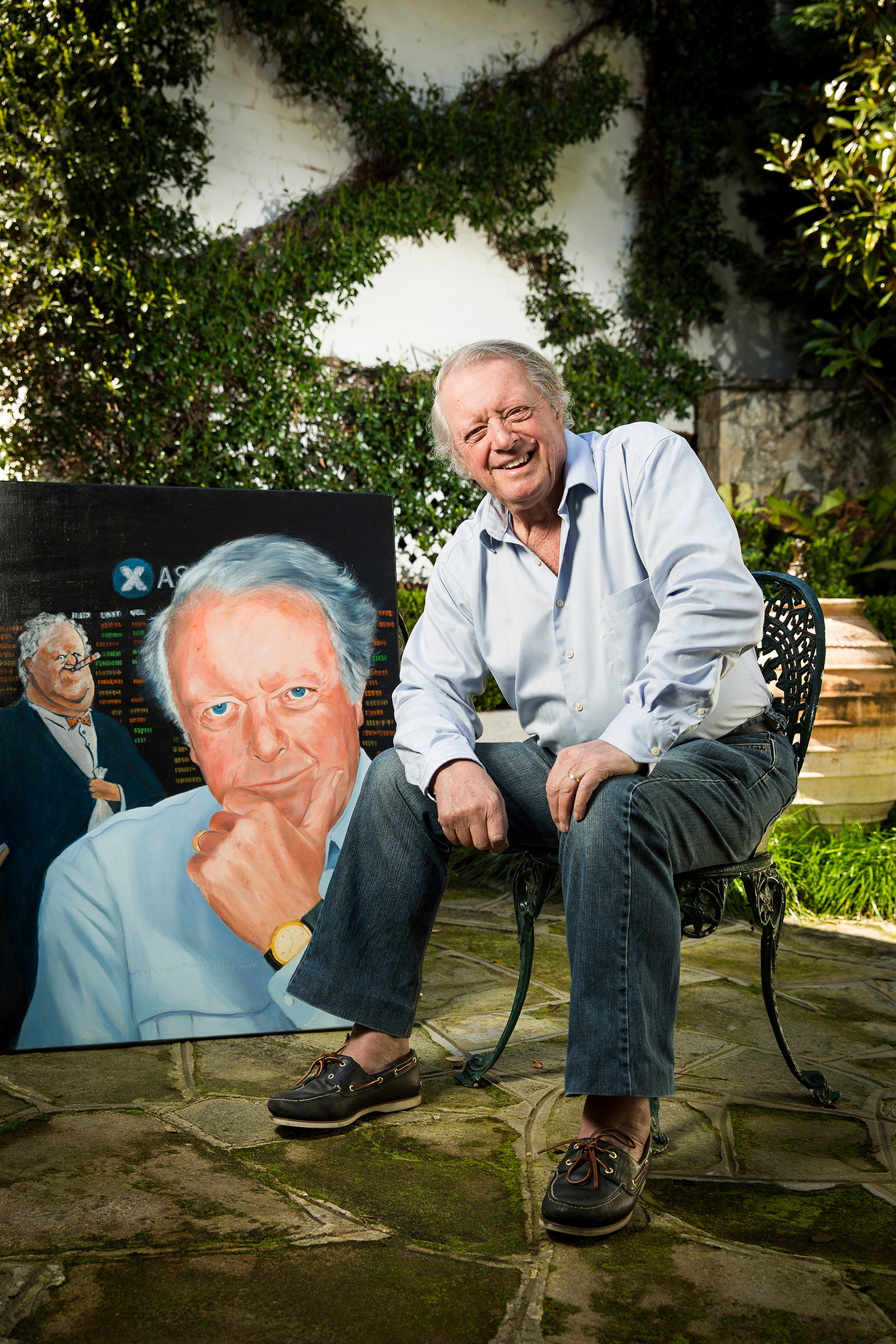 Editorial photography Trevor Sykes Australian finance journalist seated in garden with a painted self portrait in background