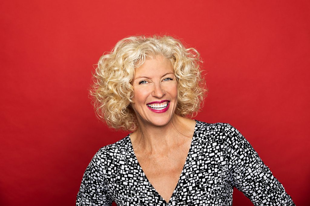Studio portrait photography of smiling female Kim Skildum-Reid on red background