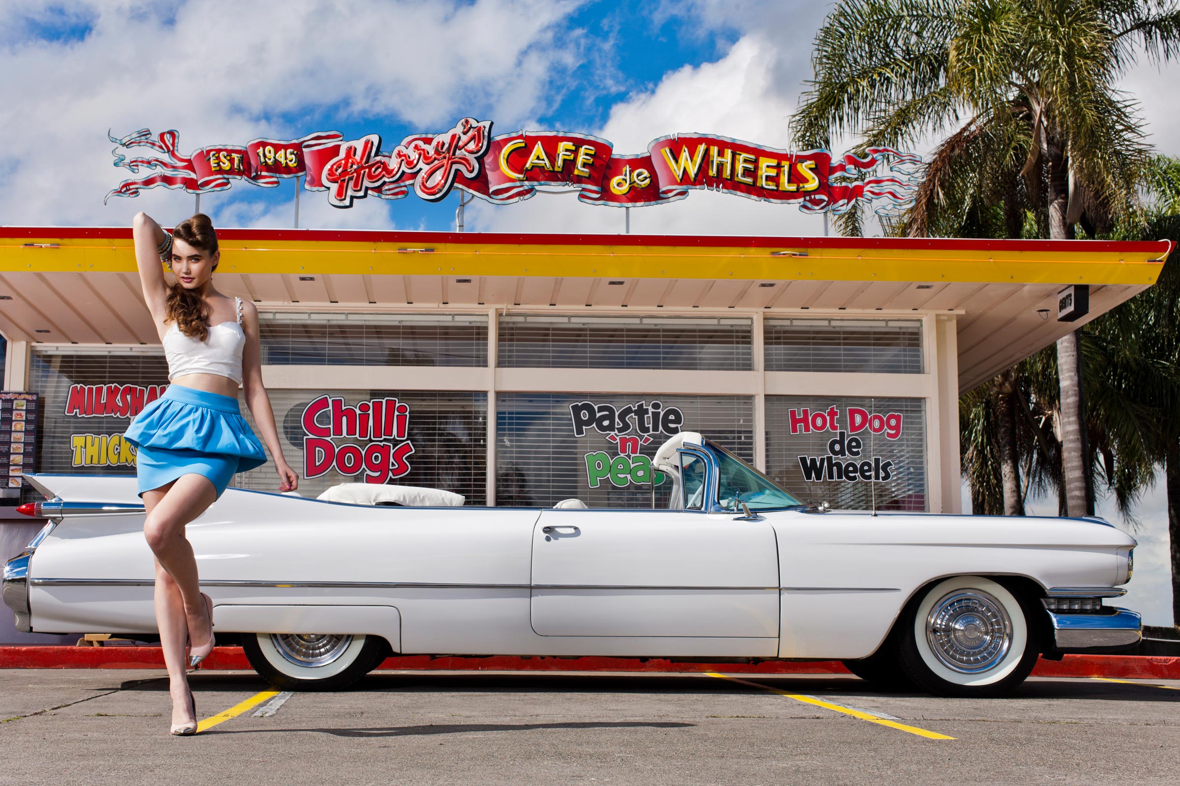 Fashion photography of female model with white convertible Cadillac and Harry Cafe de Wheels in the background