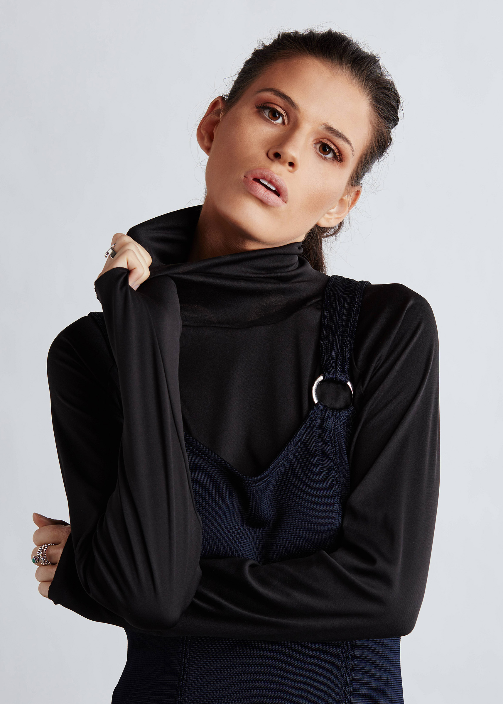 Studio fashion photography of female model wearing black jumper and overalls pulling on collar
